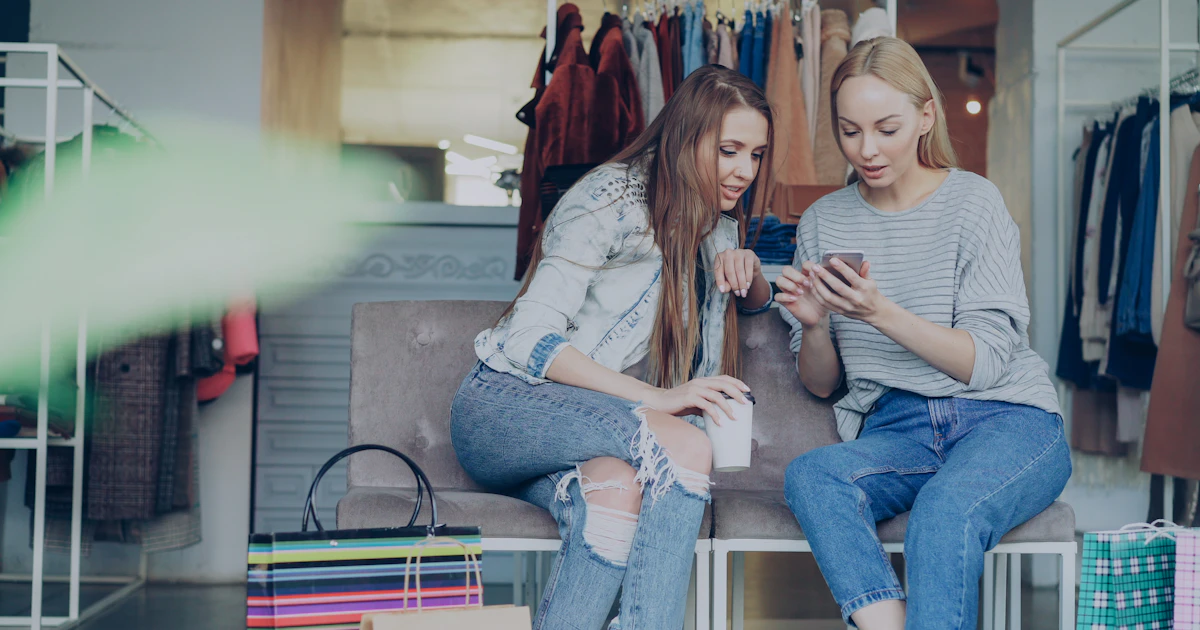 Due clienti guardano lo smartphone mentre si trovano in un negozio di abbigliamento