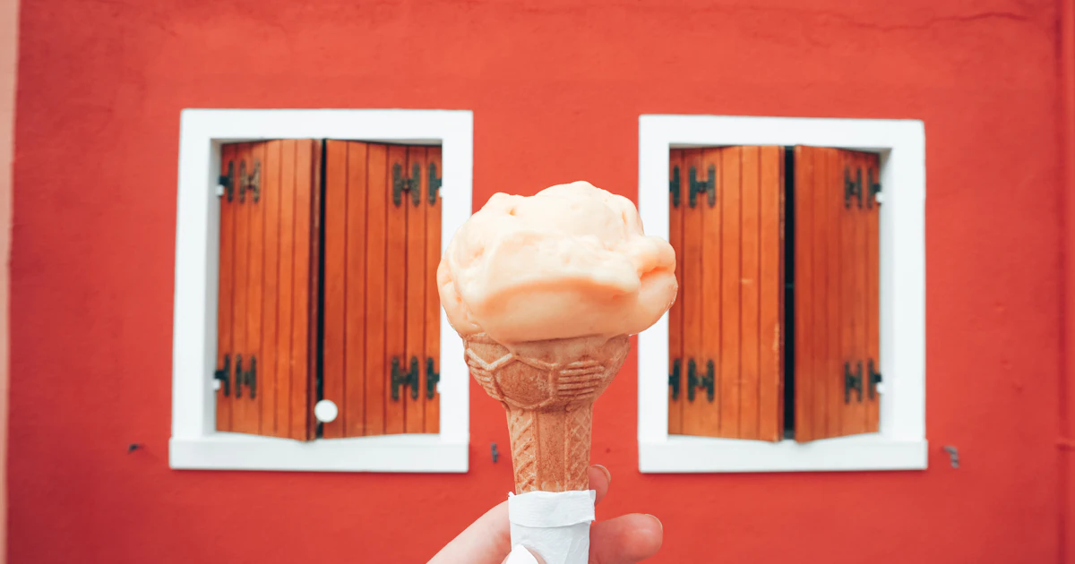 Una mano regge un cono gelato in una via italiana estiva: il consumatore italiano in modalità saldi è in vacanza, in viaggio, fuori dal negozio