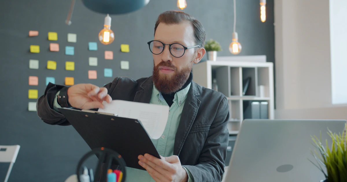 Direttore con occhiali studia documenti alla scrivania davanti al laptop